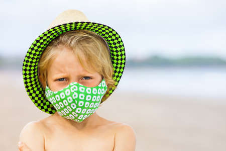 Child in straw hat, stylish masks have fun on sea beach. New rules to wear face covering at public places.の写真素材