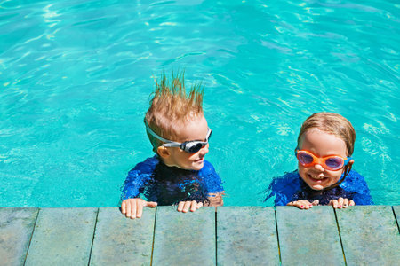 Happy children in wetsuits and goggles learn to swim, have fun at poolside in swimming pool Healthy family lifestyle, little kids water sports activity, swimming lessons with parents at training classの写真素材
