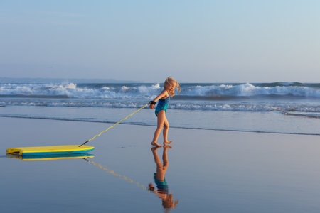 Little baby girl - young surfer with bodyboard has fun on sea beach.の写真素材