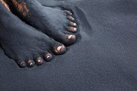 Photo of dirty woman bare feet in black sand. People relaxation, fun and walking barefoot by black volcanic sand on ocean beach. Travel lifestyle, family summer vacation on tropical island.の写真素材
