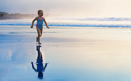 Happy family have fun on tropical sea beach resort. Funny baby girl run with splashes by water pool along surf edge. Active kids lifestyle, people swimming activity on summer holiday with children.の写真素材