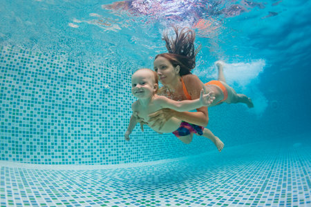 Happy family - mother, father with baby boy swimming, diving underwater with fun in blue pool. Healthy lifestyle, active parents, people water sports activity on summer vacation with childの写真素材