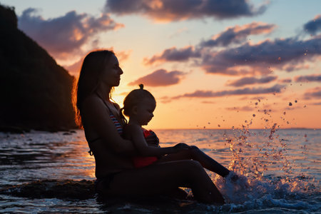Happy people have fun on summer beach holiday. Young mother with daughter relax at sea water pool. Looking at beautiful view of sunset sky. Healthy family lifestyle, summer travel on tropical island.の写真素材