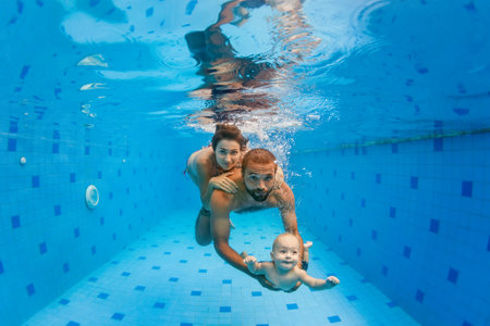 Happy family - mother, father with baby boy swimming, diving underwater with fun in blue pool. Healthy lifestyle, active parents, people water sports activity on summer vacation with childの写真素材