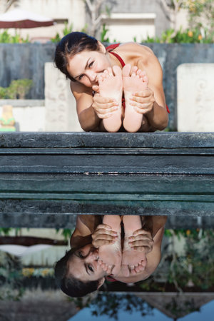 Active woman in bikini practicing yoga, stretching at villa poolside to keep fit, health. Sit in bending pose with hands outstretched to feet. Woman fitness, sport activity on summer family holidayの写真素材