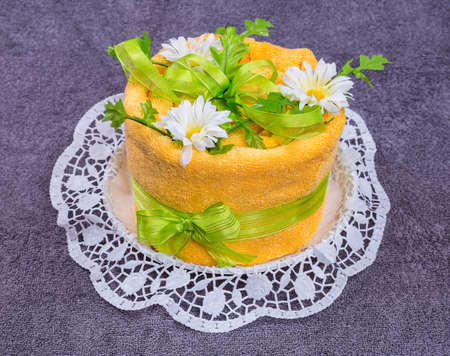 Towel cake gift  was homemade from one towel and a flowers on grey coloured background for the purpose a gift or as a beautiful decoration.の写真素材