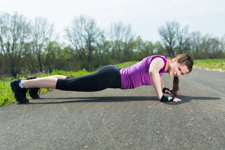 Young woman doing push ups training fitness outside on the road .