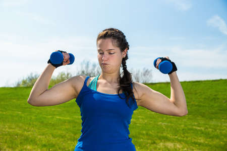 Young woman in sportswear doing responsibly fitness exercise with two dumbbells .