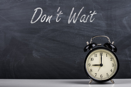 Retro alarm clock and text "Don't Wait" written with chalk on the blackboard.の写真素材