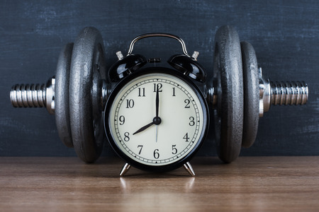 Dumbbell on a gray background and retro alarm clock. Time 8:00の写真素材
