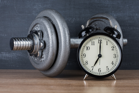 Dumbbell on a gray background and retro alarm clock. Time 7:00の写真素材