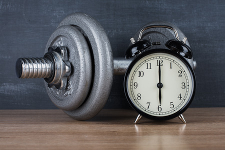 Dumbbell on a gray background and retro alarm clock. Time 6:00の写真素材