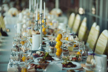 Wedding. Banquet. The chairs and table for guests, decorated with candles, served with cutlery and crockery and covered with a tablecloth. The table stands on a green lawn in the backyard banquet areaの写真素材