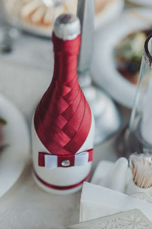 Two decorated bottles of champagne and brandy as bride and groom on wedding dinner tableの写真素材