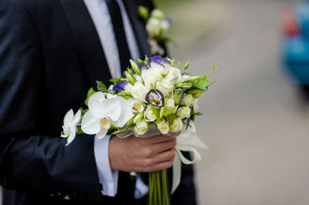 Wedding groom with bride's bouquet of flowers outside