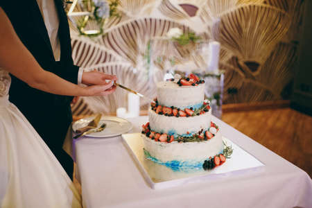 Beautiful white and colored wedding cake. A bride and a groom is cutting their wedding cakeの写真素材