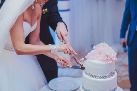 Beautiful white and colored wedding cake. A bride and a groom is cutting their wedding cakeの写真素材