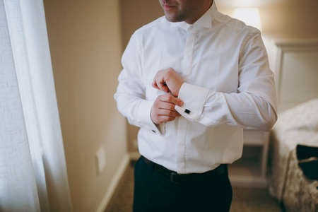 The groom fastens the cufflink on the shirt sleeve close-upの写真素材