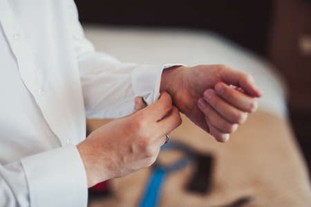 The groom fastens the cufflink on the shirt sleeve close-upの写真素材