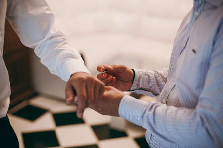 The groom fastens the cufflink on the shirt sleeve close-upの写真素材