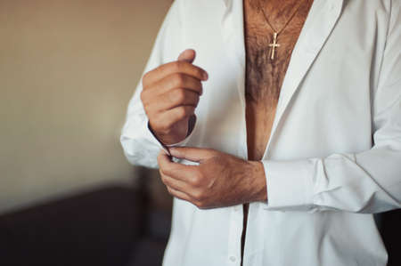 The groom fastens the cufflink on the shirt sleeve close-upの写真素材