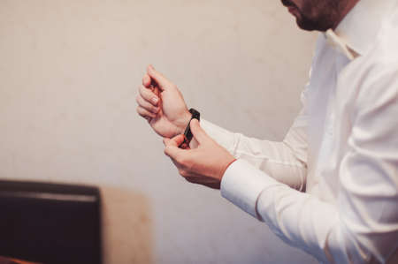 The groom fastens the cufflink on the shirt sleeve close-upの写真素材