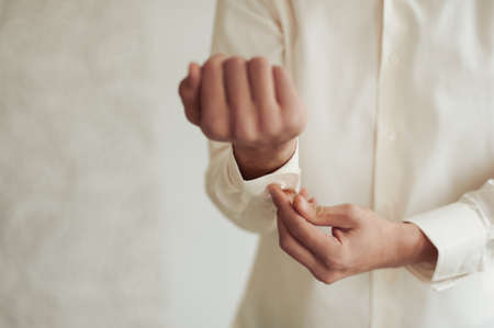 The groom fastens the cufflink on the shirt sleeve close-upの写真素材