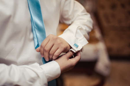 The groom fastens the cufflink on the shirt sleeve close-upの写真素材