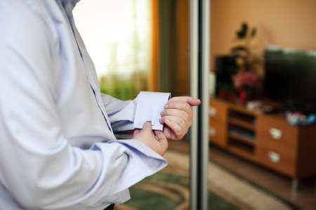 The groom fastens the cufflink on the shirt sleeve close-upの写真素材