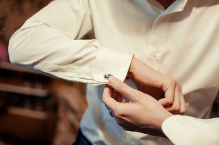 The groom fastens the cufflink on the shirt sleeve close-upの写真素材
