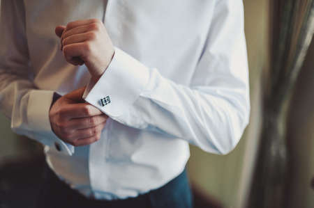 The groom fastens the cufflink on the shirt sleeve close-upの写真素材