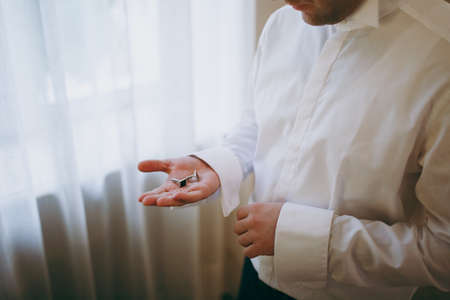 The groom fastens the cufflink on the shirt sleeve close-upの写真素材