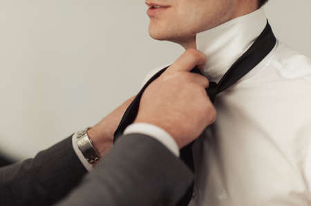 The groom puts on his tie. A business man is dressing a tie.の写真素材