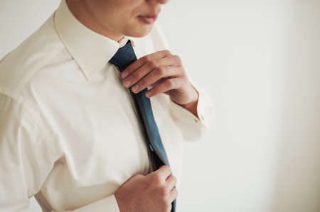 The groom puts on his tie. A business man is dressing a tie.の写真素材