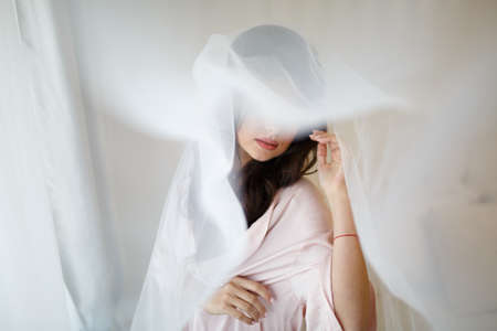 Closeup shot of elegant, brunette bride in vintage white dress posing under veil closeup. Bride portrait wedding makeup and hairstyle with diamond crown, fashion bride. Beautiful bride in veilの写真素材