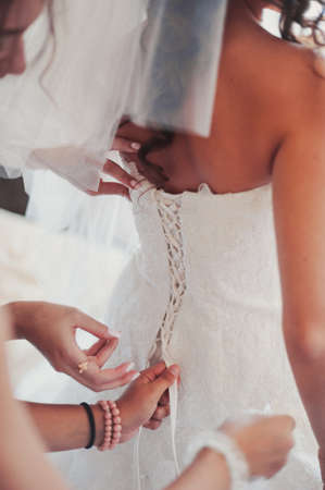 Fashionable bridesmaids dresses helped wear bow on back of wedding dress bride. Morning wedding day.の写真素材