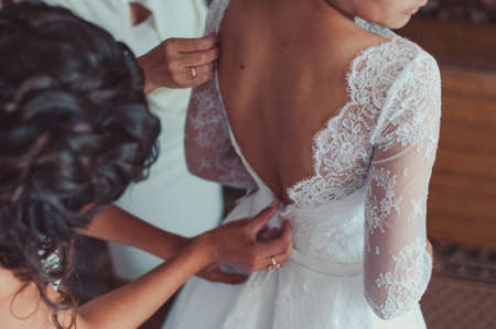 Fashionable bridesmaids dresses helped wear bow on back of wedding dress bride. Morning wedding day.の写真素材