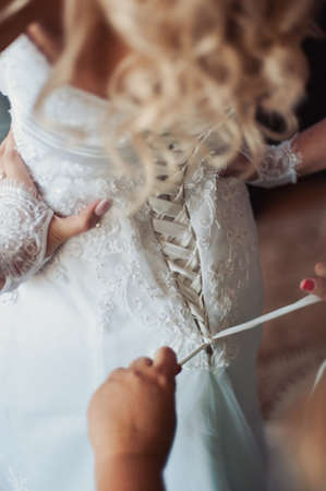 Fashionable bridesmaids dresses helped wear bow on back of wedding dress bride. Morning wedding day.の写真素材