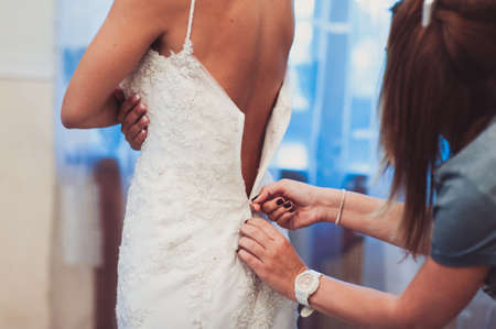 Fashionable bridesmaids dresses helped wear bow on back of wedding dress bride. Morning wedding day.の写真素材