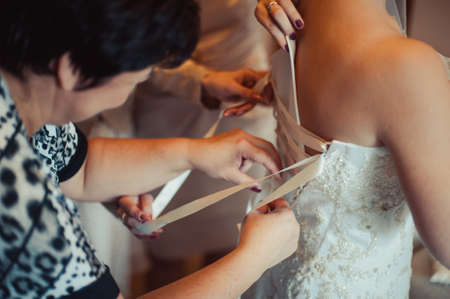 Fashionable bridesmaids dresses helped wear bow on back of wedding dress bride. Morning wedding day.の写真素材