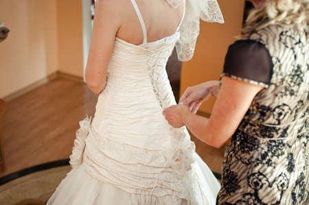 Fashionable bridesmaids dresses helped wear bow on back of wedding dress bride. Morning wedding day.の写真素材