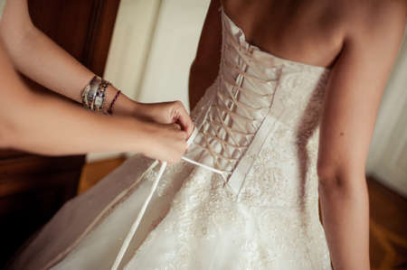 Fashionable bridesmaids dresses helped wear bow on back of wedding dress bride. Morning wedding day.の写真素材