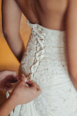 Fashionable bridesmaids dresses helped wear bow on back of wedding dress bride. Morning wedding day.の写真素材