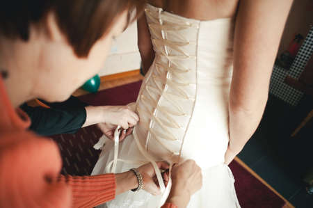 Fashionable bridesmaids dresses helped wear bow on back of wedding dress bride. Morning wedding day.の写真素材