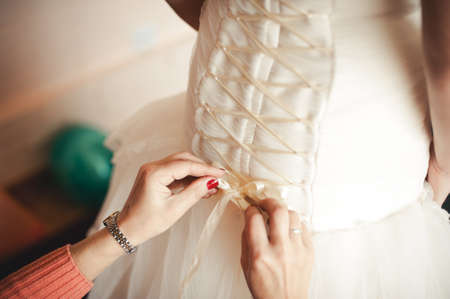 Fashionable bridesmaids dresses helped wear bow on back of wedding dress bride. Morning wedding day.の写真素材