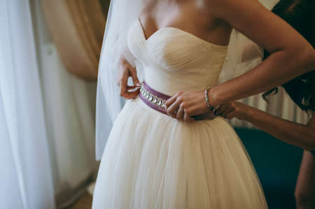 Fashionable bridesmaids dresses helped wear bow on back of wedding dress bride. Morning wedding day.の写真素材