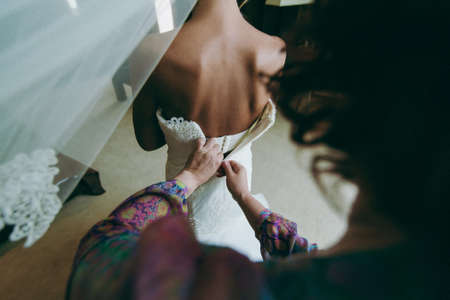 Fashionable bridesmaids dresses helped wear bow on back of wedding dress bride. Morning wedding day.の写真素材