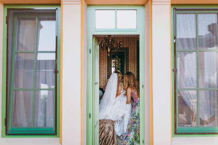 Fashionable bridesmaids dresses helped wear bow on back of wedding dress bride. Morning wedding day.の写真素材