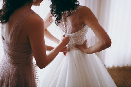 Fashionable bridesmaids dresses helped wear bow on back of wedding dress bride. Morning wedding day.の写真素材