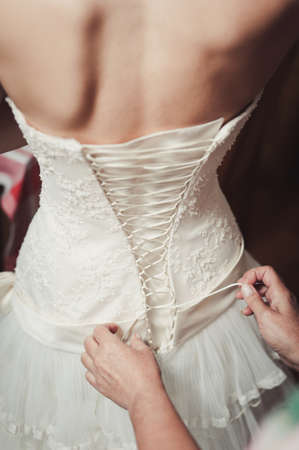 Fashionable bridesmaids dresses helped wear bow on back of wedding dress bride. Morning wedding day.の写真素材